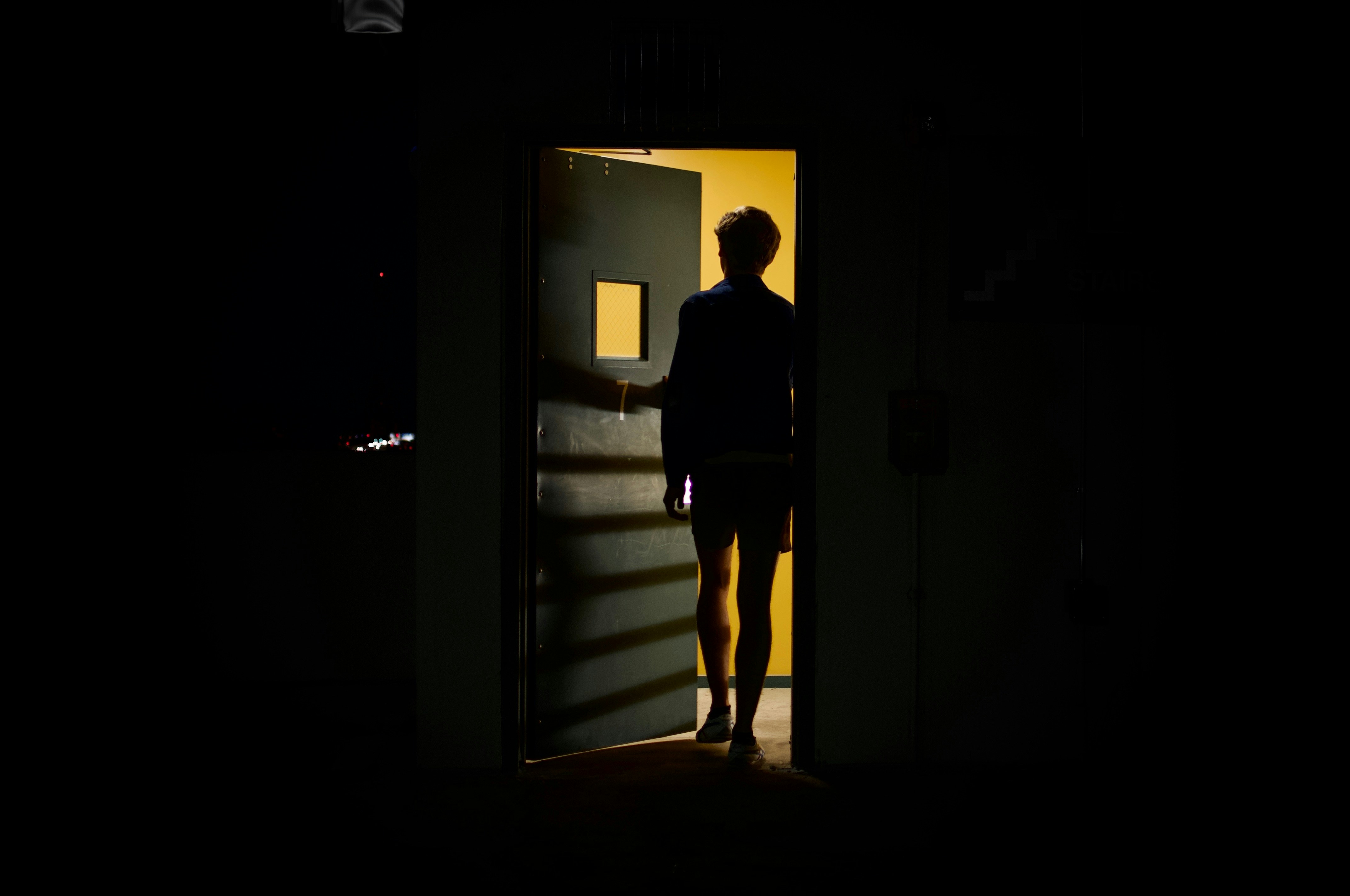 Photo couleur d'un espace obscur avec une porte au fond qui s'ouvre et silhouette de dos 